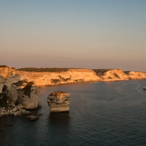 Falaises calcaires de Bonifacio dans la lumière rasante du soir, avec le rocher isolé du Grain de Sable au premier plan (août 2016).