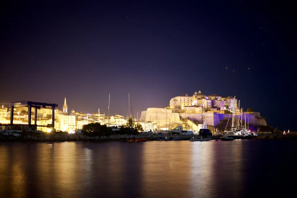 La citadelle de Calvi illuminée la nuit, reflets sur l'eau du port (août 2016).