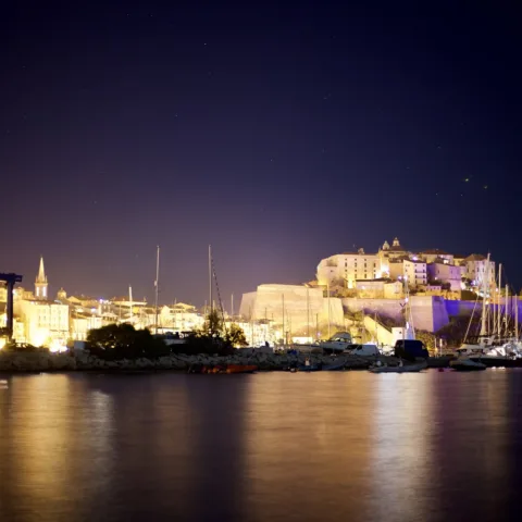La citadelle de Calvi illuminée la nuit, reflets sur l'eau du port (août 2016).