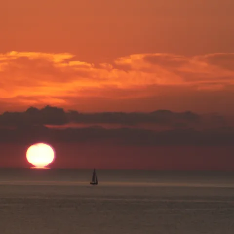 Lever du soleil sur la mer au large de Pinarellu (côte orientée à l'est), un voilier à l'horizon (juillet 2008).