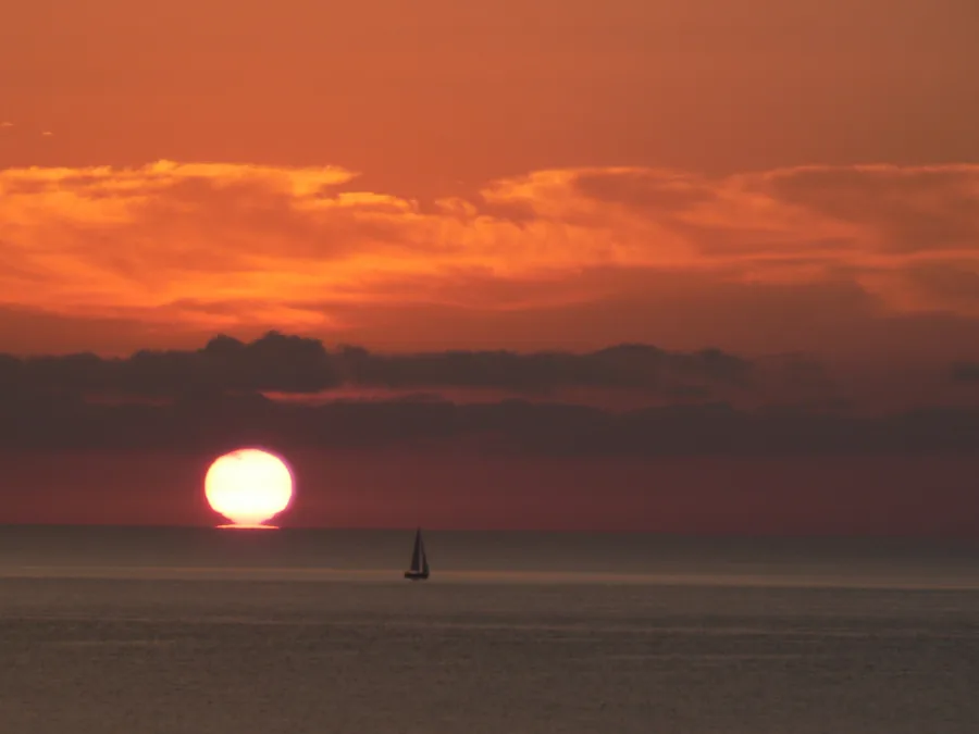 Lever du soleil sur la mer au large de Pinarellu (côte orientée à l'est), un voilier à l'horizon (juillet 2008).
